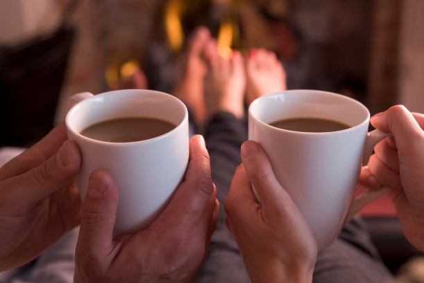 Feet warming at fireplace with hands holding coffee